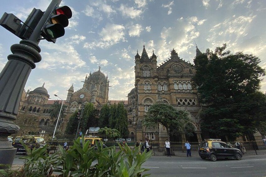 A historic building with intricate architecture, a traffic light, and a street with vehicles and pedestrians. 1