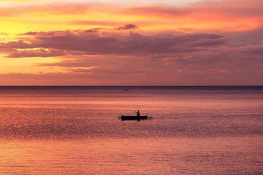 A sunset over a calm sea with a small boat in the distance. 1