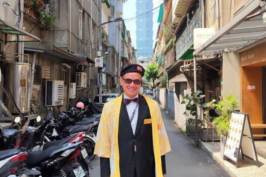 A narrow street with parked motorcycles, a person in a yellow robe, and a deli sign. 2