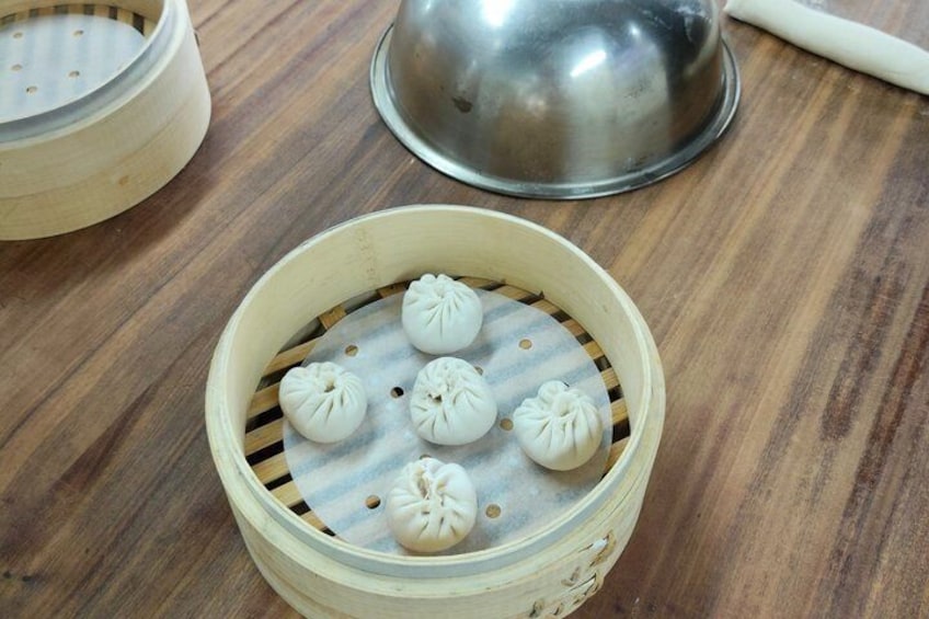 A bamboo steamer with several dumplings on a wooden table. 5