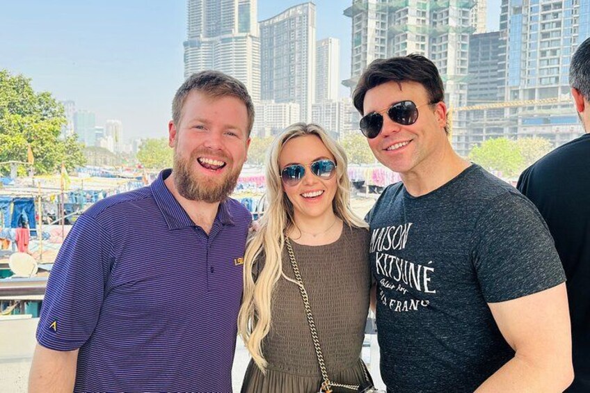 Tres personas de pie al aire libre con un horizonte urbano al fondo. 3