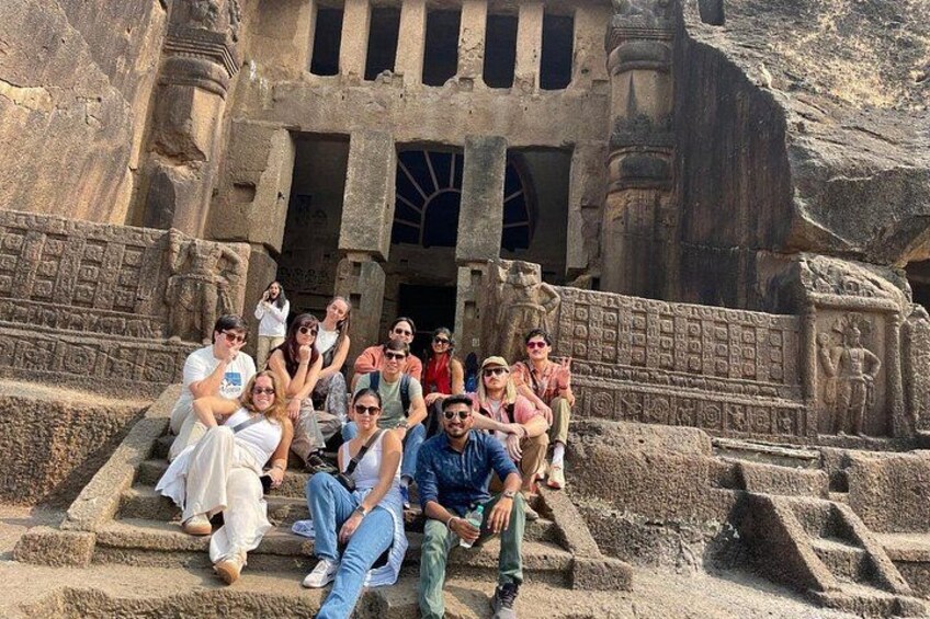 A group of people sitting on ancient stone steps in front of a large, intricately carved structure. 1