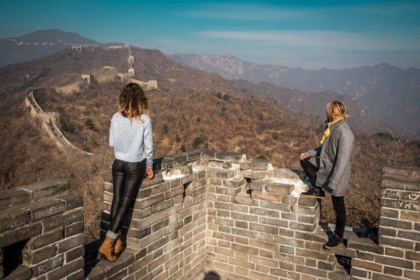 Two people standing on the Great Wall of China, overlooking the surrounding mountainous landscape. 1
