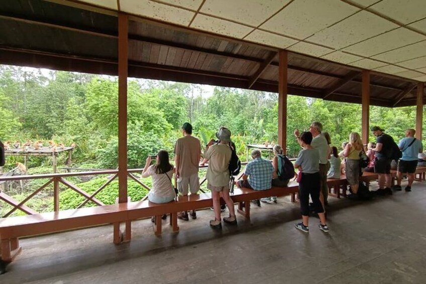 A covered outdoor area with people sitting on benches, overlooking a natural landscape. 2