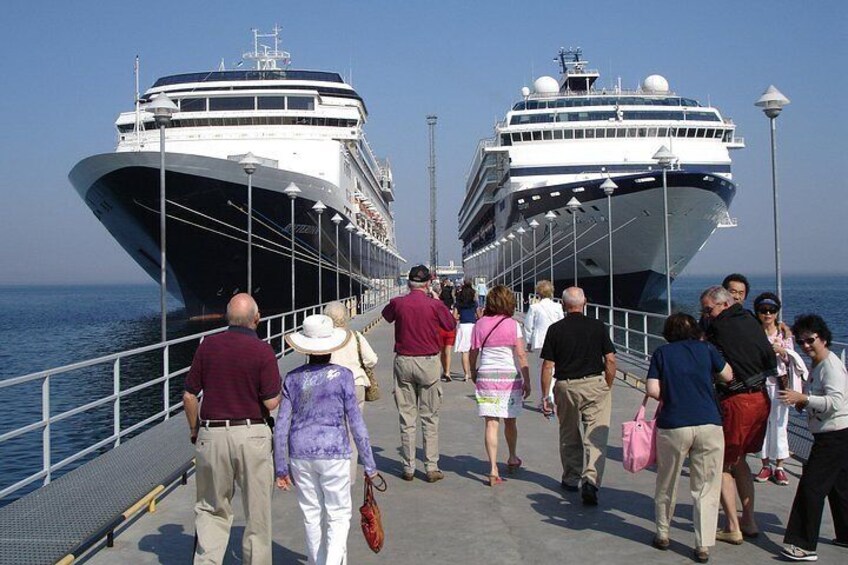 Two cruise ships docked at a pier with people walking along the pier. 1