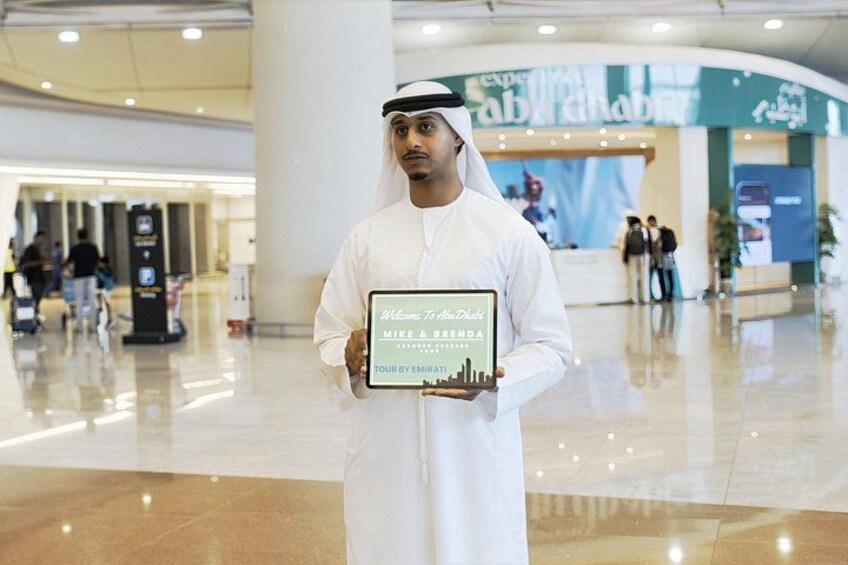 A person in traditional attire holding a plaque in a modern indoor setting with a curved ceiling and a reception area in the background. 5