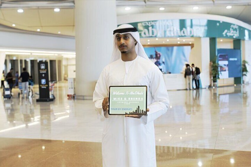 A man in traditional attire holding a plaque in a modern indoor setting with a reception area in the background. 2