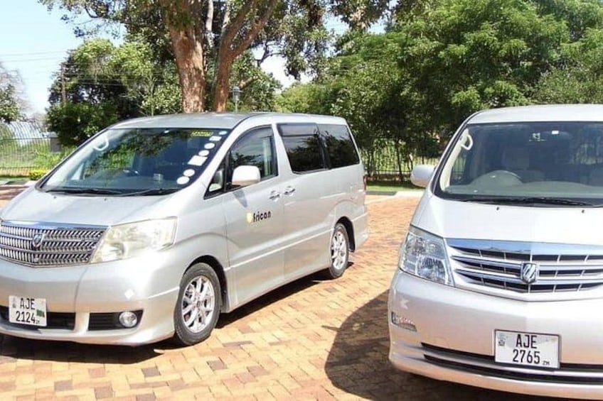 Two white vans parked on a brick surface with trees in the background. 3