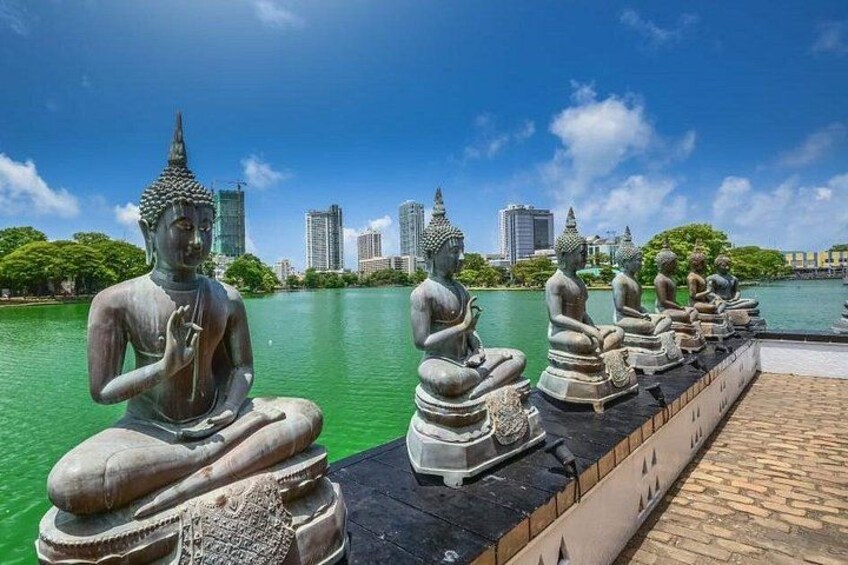 A row of Buddha statues by a waterfront with a city skyline in the background. 4