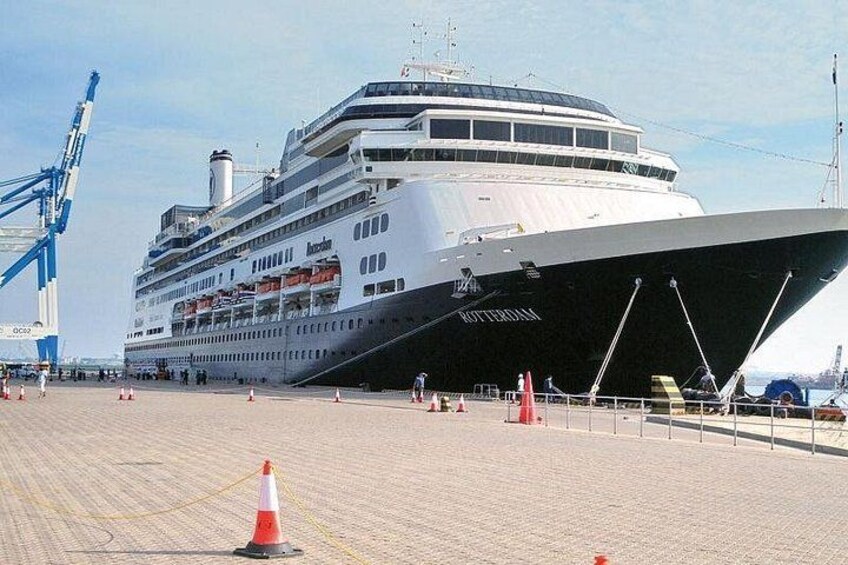 A large cruise ship docked at a port with a crane and several orange traffic cones. 2