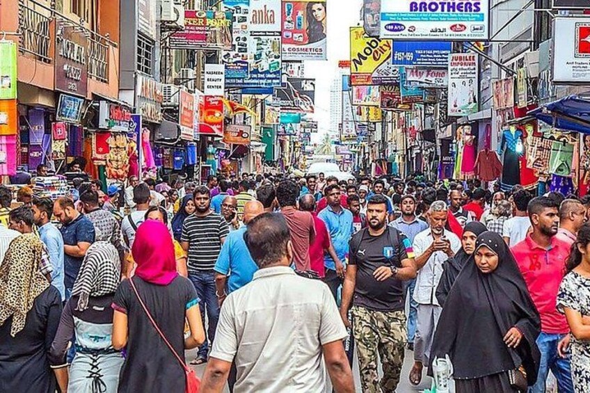 A crowded street with people walking and various shops. 1