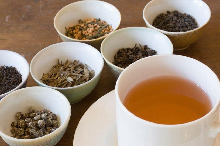A white cup of tea with seven small bowls of different tea leaves in the background. 3