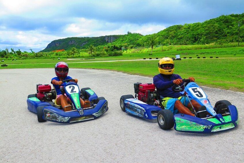 Two go-karts on a paved track with a green landscape in the background. 2