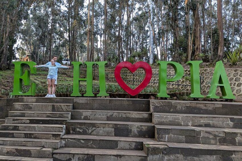 Una persona de pie en unos escalones con letras verdes grandes que deletrean 'ETHIOPIA' y un corazón rojo entre las letras. 2