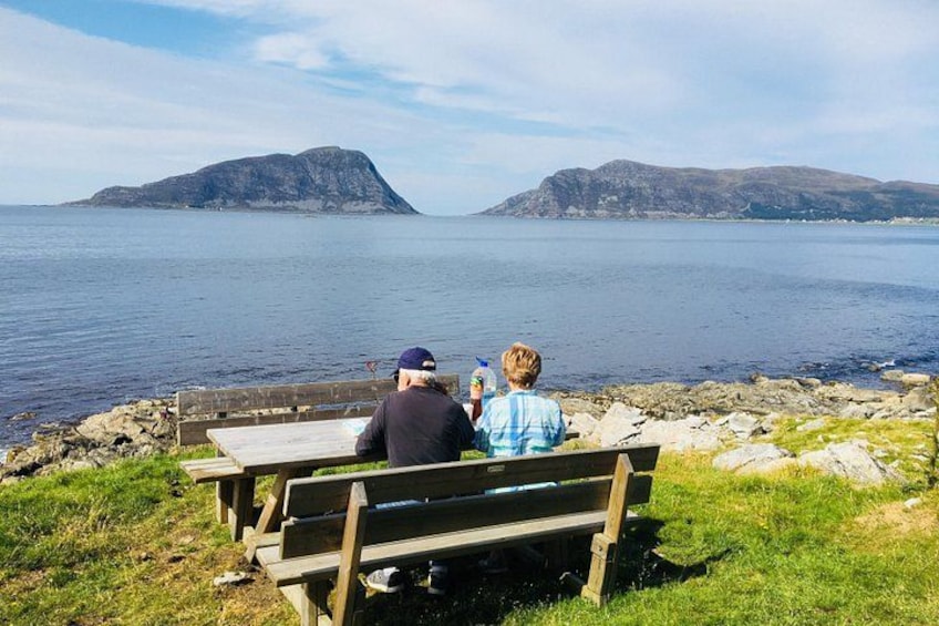 Two people sitting on a bench overlooking a calm body of water with distant islands. 3