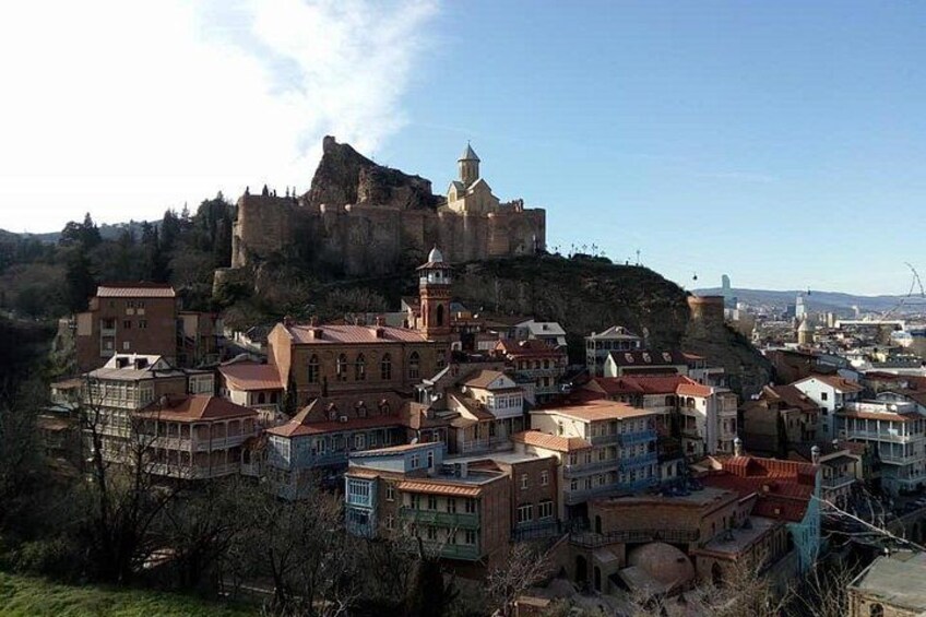 Una città storica con un castello imponente su una collina, edifici colorati e un cielo sereno. 4