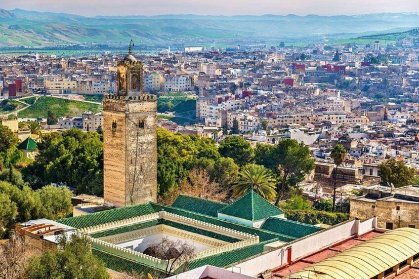 A cityscape with a prominent tower and a mosque with a green roof. 5