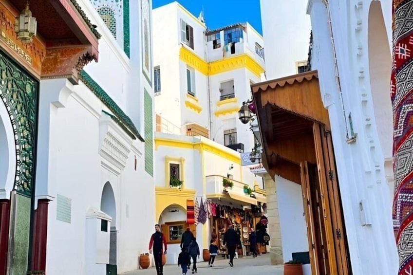 Una calle estrecha con edificios blancos, una puerta de madera y una tienda con objetos coloridos. 3