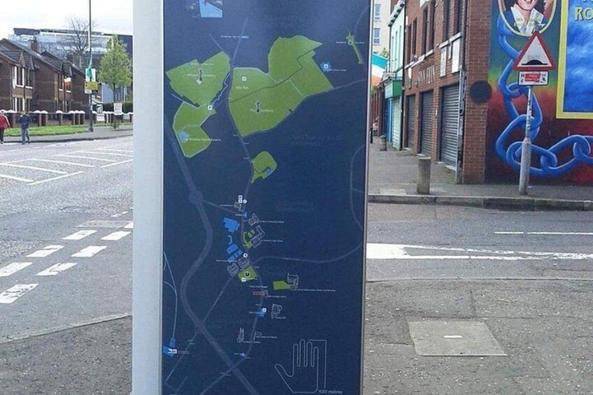 Et kort på en stang, en vej med et fodgængerfelt og en bygning med et muralmaleri. 3