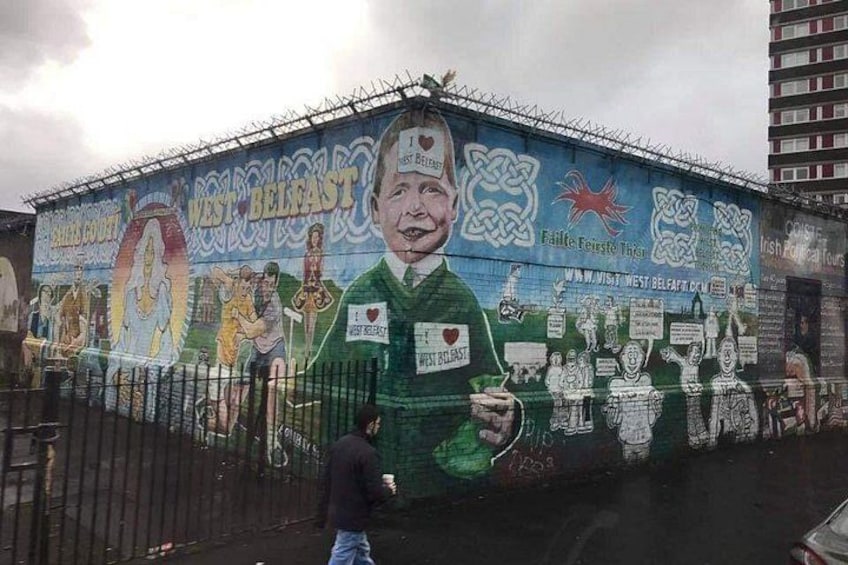 A mural on a building with a man holding a heart-shaped object, surrounded by various symbols and text. 2