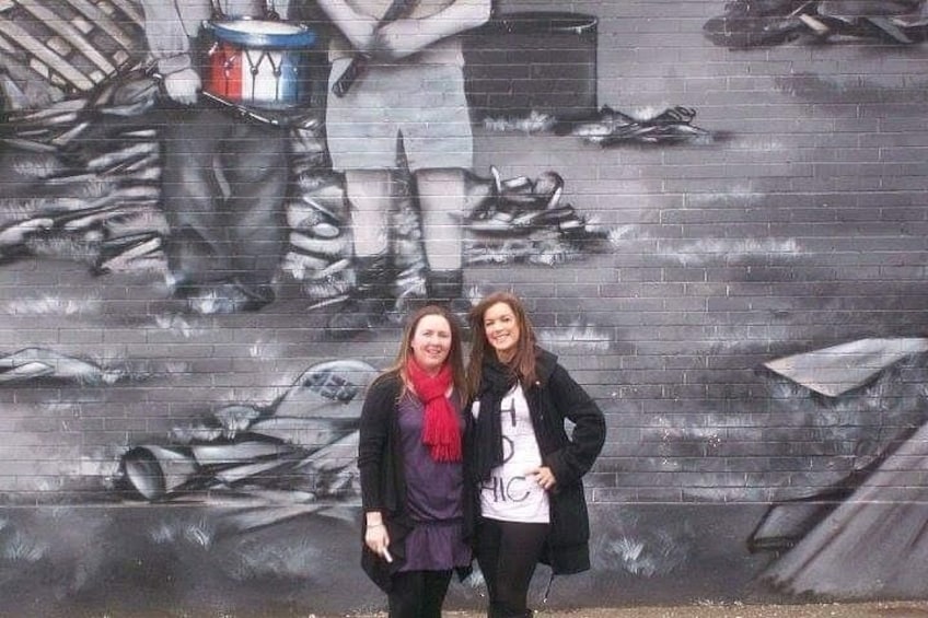 Two people standing in front of a mural with fish and a person in a bucket. 5