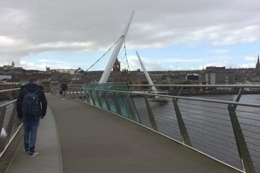 A pedestrian bridge with a modern design, a river below, and a cityscape in the background. 3