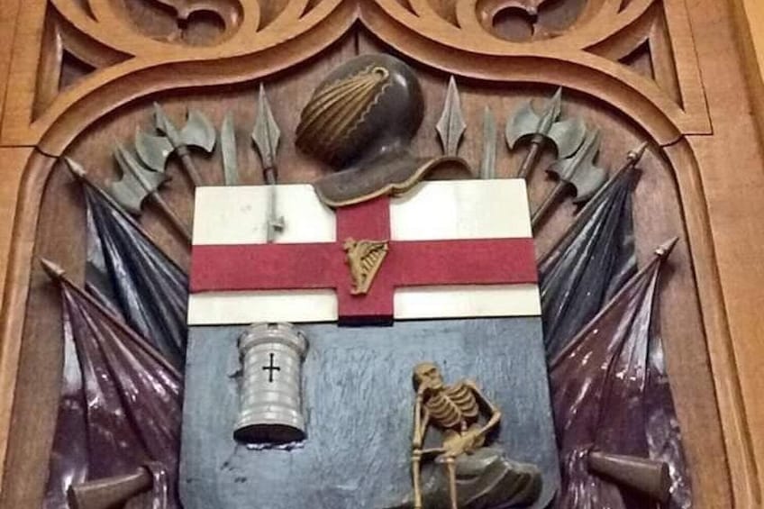 A wooden carving with a shield, a cross, and a skeleton. 4