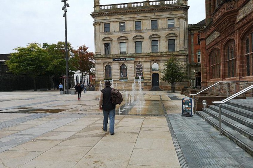 A man walking towards a building with a fountain in front. 3