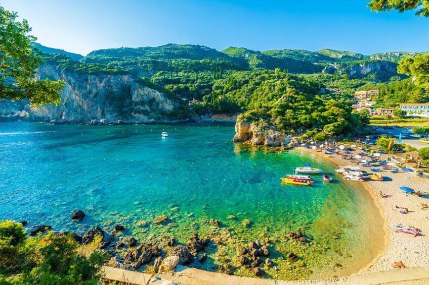 Une plage côtière bordée d’une eau turquoise et limpide, avec des bateaux et une côte rocheuse. 1