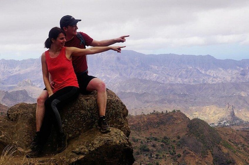 Dos personas sentadas sobre una roca, con un paisaje montañoso al fondo. 2