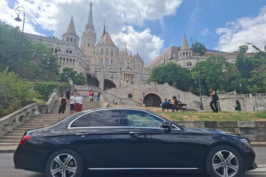 Ein schwarzes Auto parkt vor einem historischen Gebäude mit mehreren Türmen und einer Treppe, die zu ihm hinaufführt. 4
