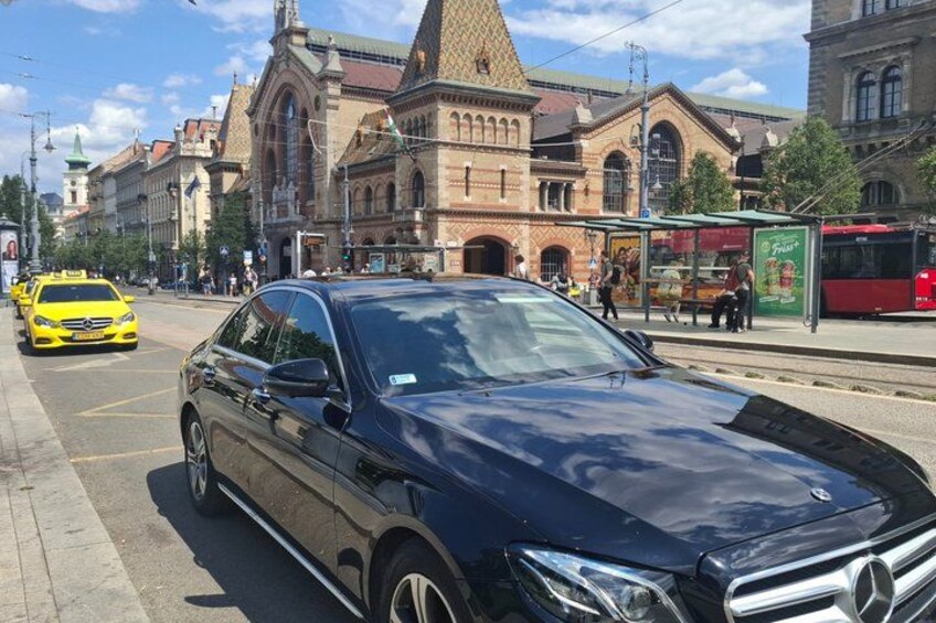 Ein schwarzes Auto steht auf einer Stadtstraße, im Hintergrund ein Straßenbahngleis und ein gelbes Taxi. 2