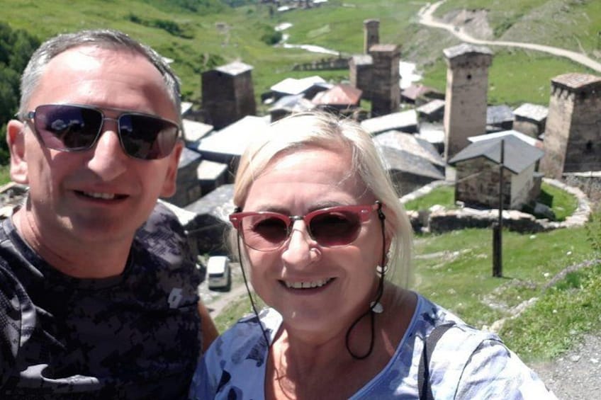 A couple standing in front of a historical site with stone structures and a green landscape. 1