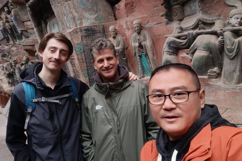 Drei Personen stehen vor einer Steinskulptur mit Figuren in unterschiedlichen Posen. 3