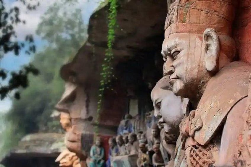 A row of stone statues with intricate carvings, set against a backdrop of trees and a clear sky. 2