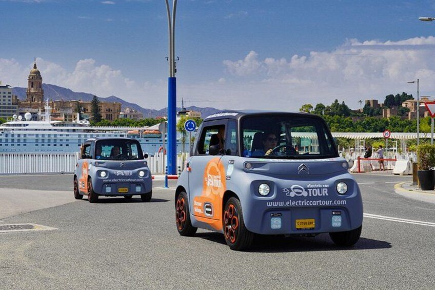 Two electric cars on a road with a bridge and a body of water in the background. 1