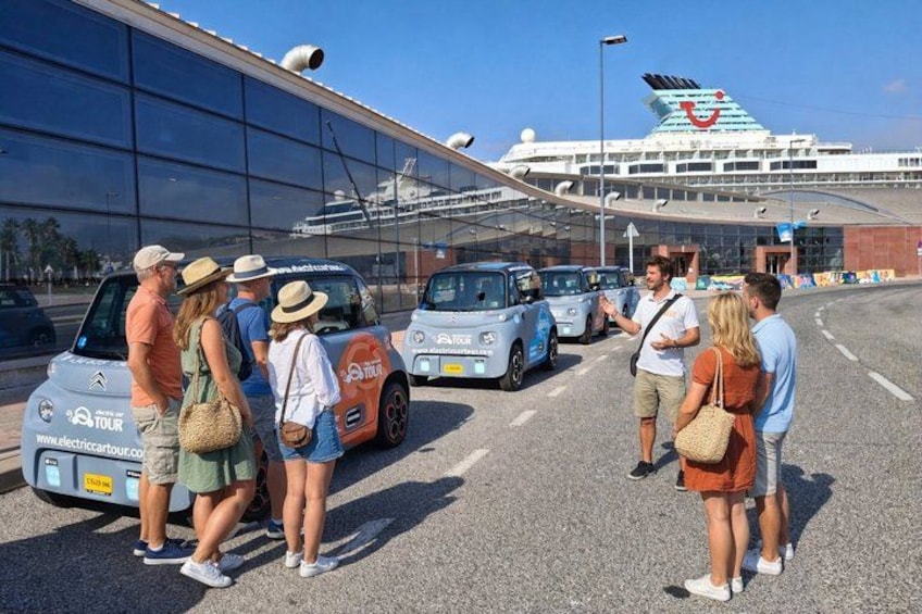 A group of people standing near a cruise ship terminal, with several tour buses parked in front. 5