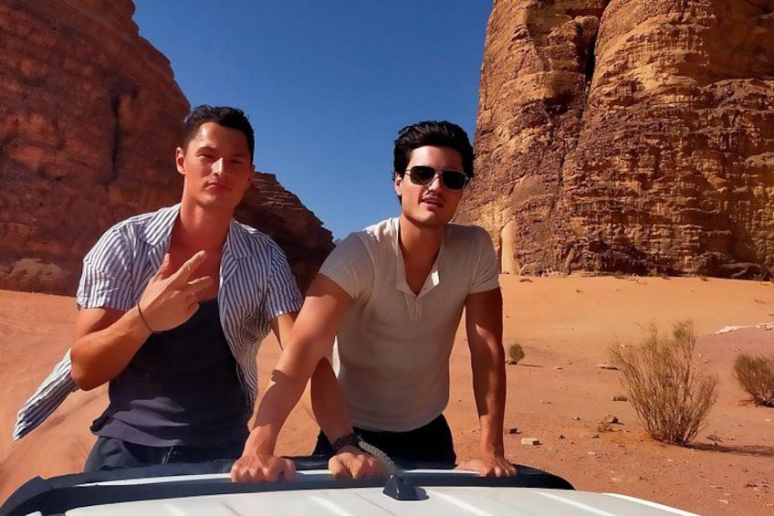 Two people standing in a desert with red rock formations in the background. 2
