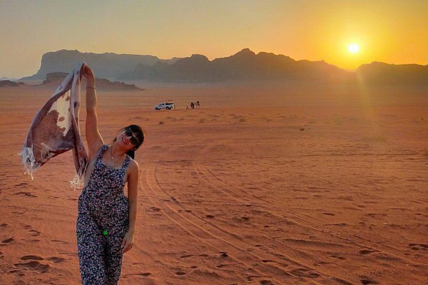 A desert landscape with a person holding a scarf, a vehicle, and mountains in the background. 1