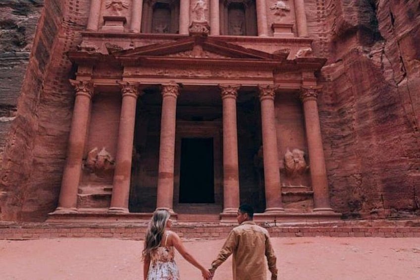 A couple holding hands in front of a large, ancient stone structure with columns. 4