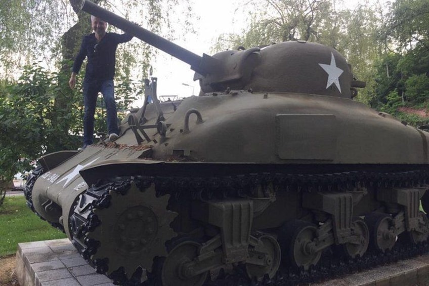 A military tank with a star insignia, a person standing next to it, and trees in the background. 3