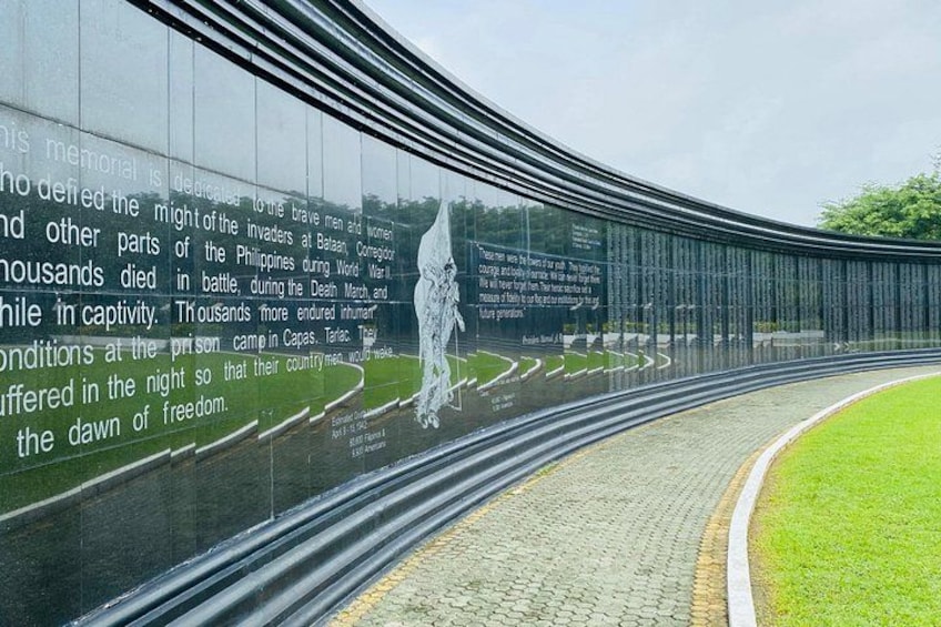 A curved glass memorial with engraved text and a silhouette of a soldier. 1