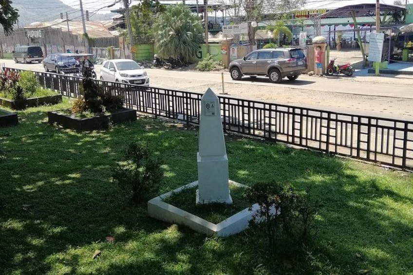 A grassy area with a white monument, a black metal fence, and a road with cars and a motorcycle. 5