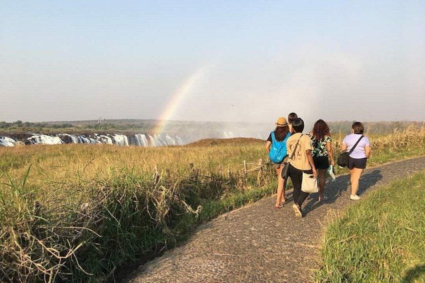 A group of people walking on a path with a waterfall and a rainbow in the background. 2