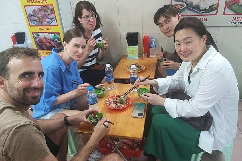 A group of people sitting around a table with food, water bottles, and chopsticks. 5