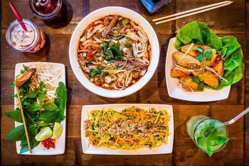 Variedad de platos vietnamitas, incluyendo un tazón de sopa de fideos, un plato de rollitos primavera, un plato con fideos y hierbas, y una ensalada de fideos. 4