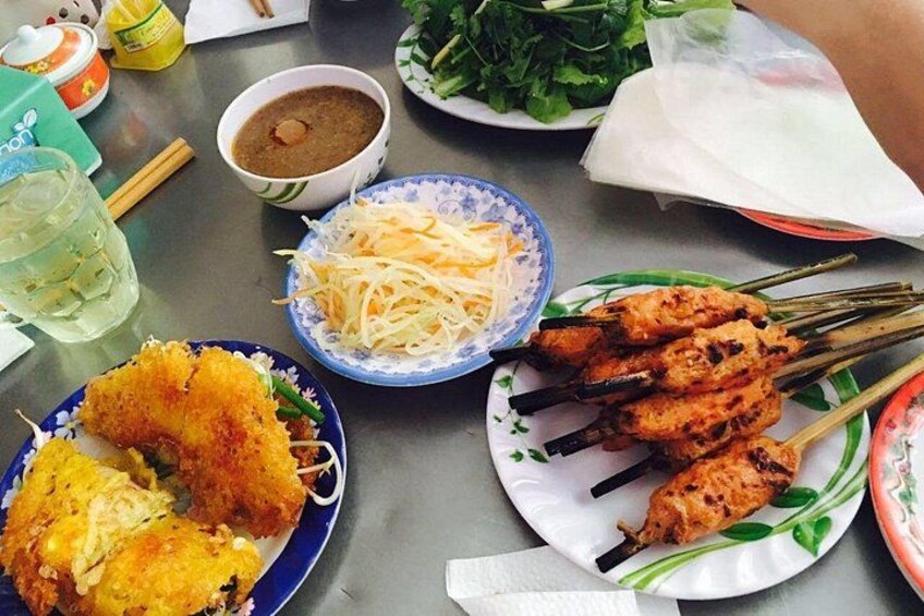 A table with various dishes including skewered meat, fried items, and a bowl of soup. 3