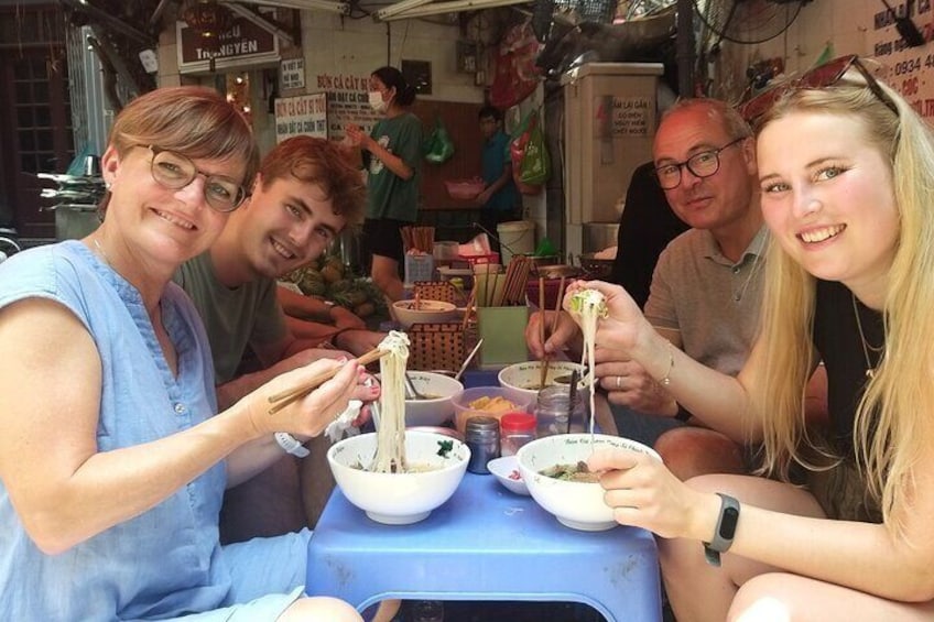 A group of people eating noodles at a street food stall. 4
