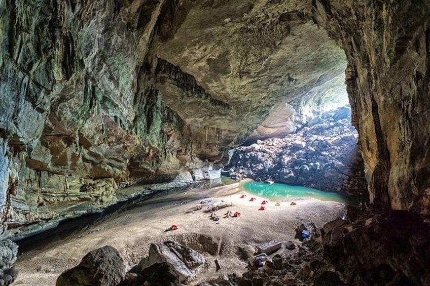 A cave with a beach inside, featuring rock formations and a turquoise pool. 1