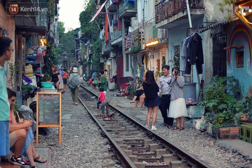 Vías de tren con personas de pie, rodeadas de edificios y follaje. 5